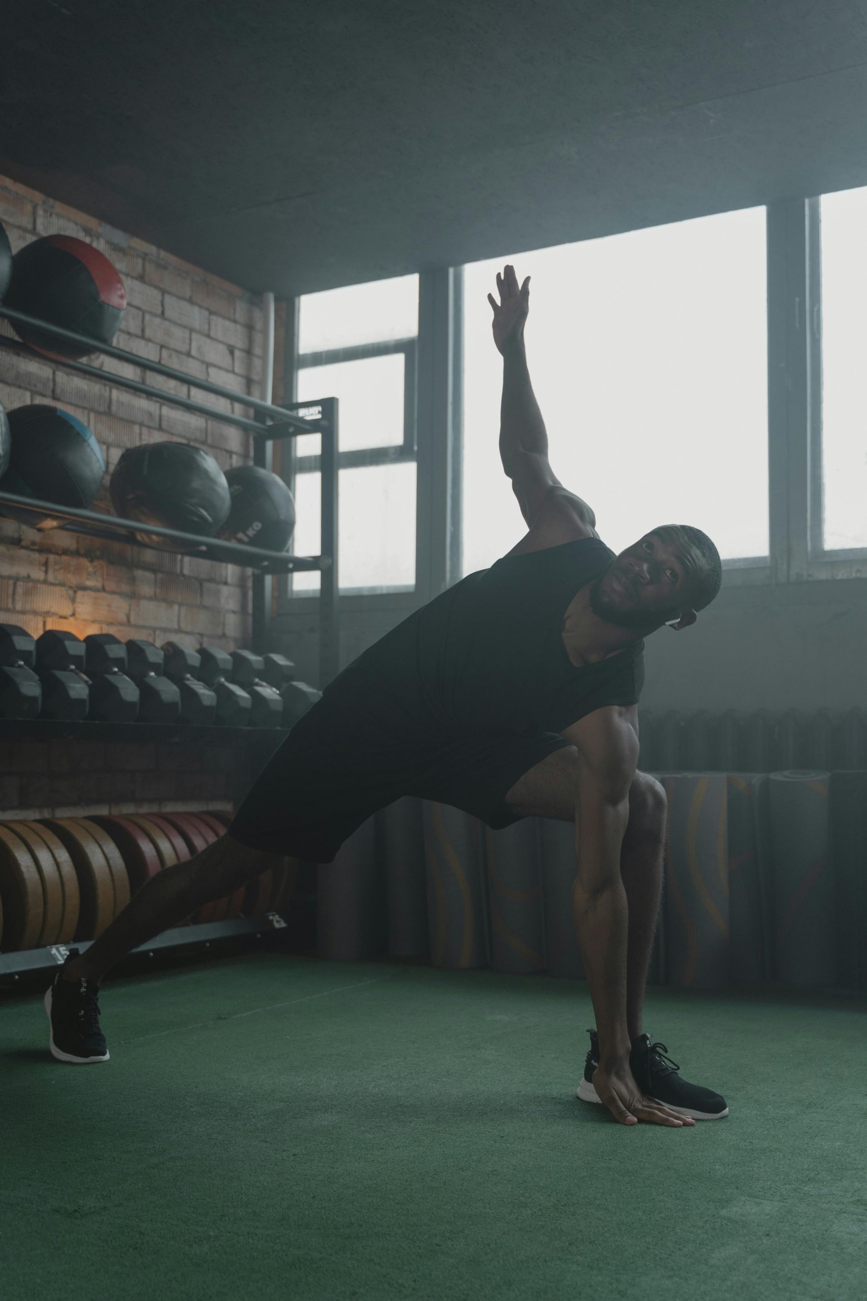 An athletic man performs a stretching exercise in a gym surrounded by fitness equipment.